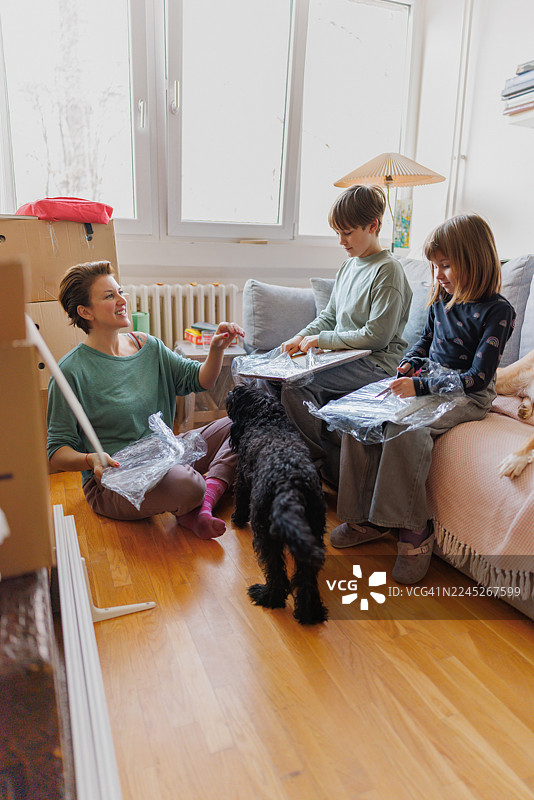 女人坐在地板上，旁边是狗，孩子们坐在沙发上，房间里堆满了箱子图片素材