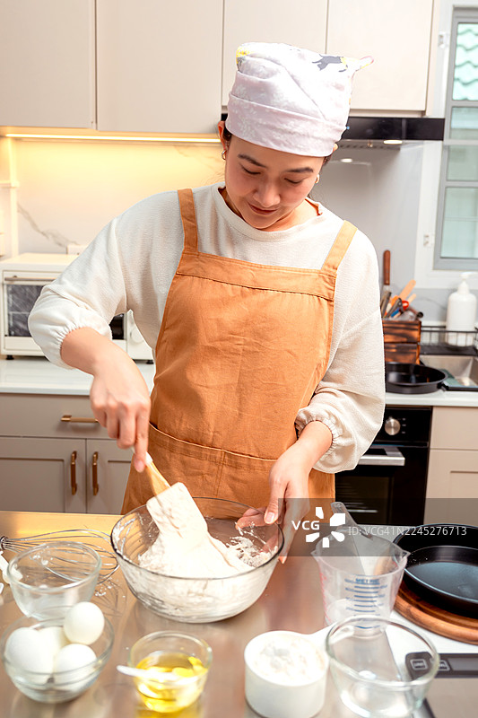 亚洲女性在家里的厨房为节日家庭聚会烹饪自制披萨。图片素材