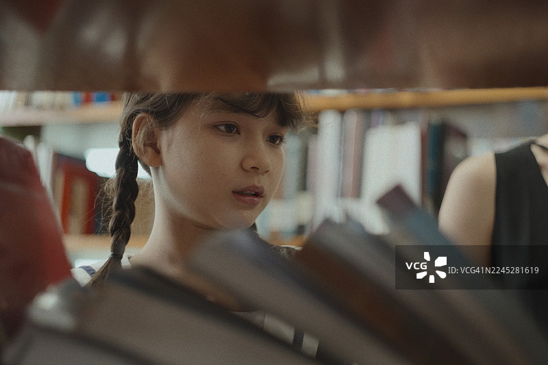 亚洲小学生和老师在学习时间一起在学校图书馆挑选要读的书。图片素材