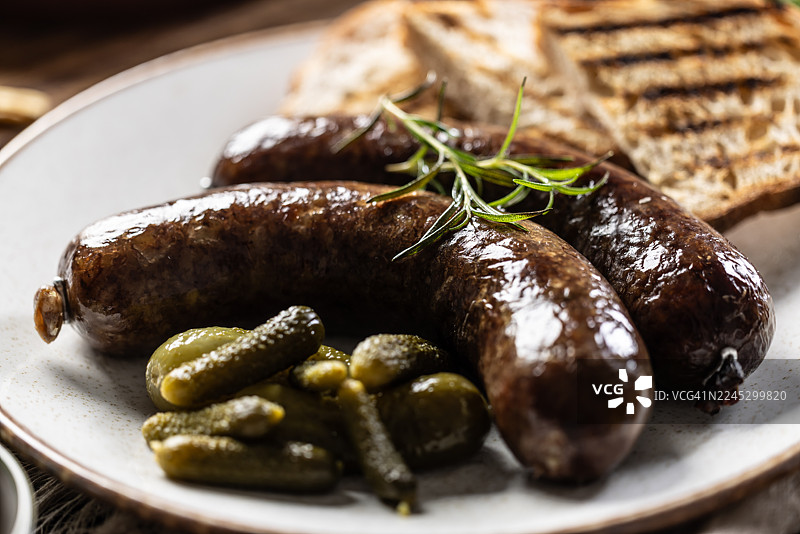 烤香肠配面包、腌黄瓜和香草放在盘子上。传统欧洲美食，如布拉特香肠、捷克香肠或捷克香肠。图片素材