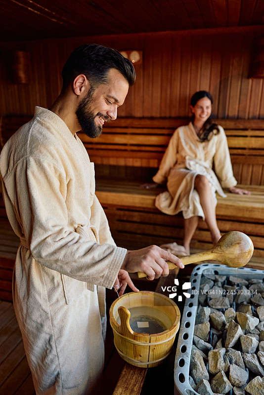 一对情侣在桑拿房放松，往热石上加水图片素材
