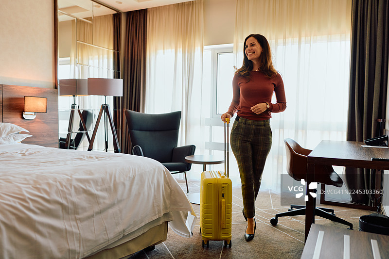 一位女商人拖着行李箱抵达酒店房间，准备进行商务旅行图片素材