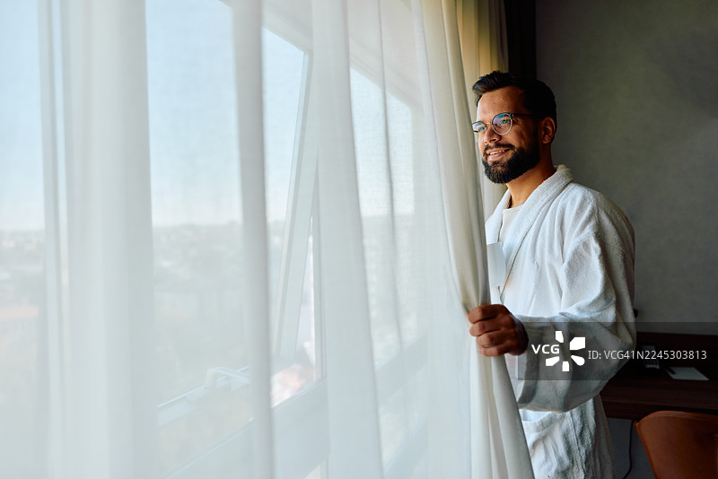 年轻的成年男子在早晨拉开酒店房间的窗帘图片素材