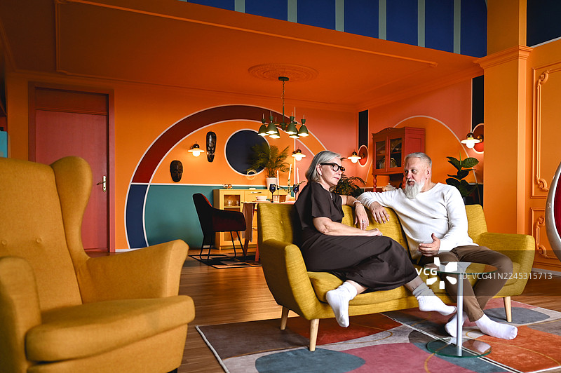 一对年长的夫妇在色彩鲜艳的复古客厅沙发上放松图片素材
