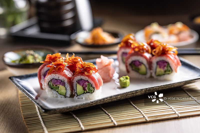 六块反卷寿司摆放在时尚的盘子里，寿司卷包裹着金枪鱼，上面点缀着闪亮的琥珀色配料，很可能是焦糖洋葱。图片素材
