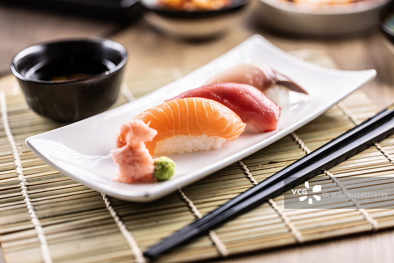 特写镜头，盘中盛放着精致的寿司，摆放在竹席上的长方形白盘里。图片素材