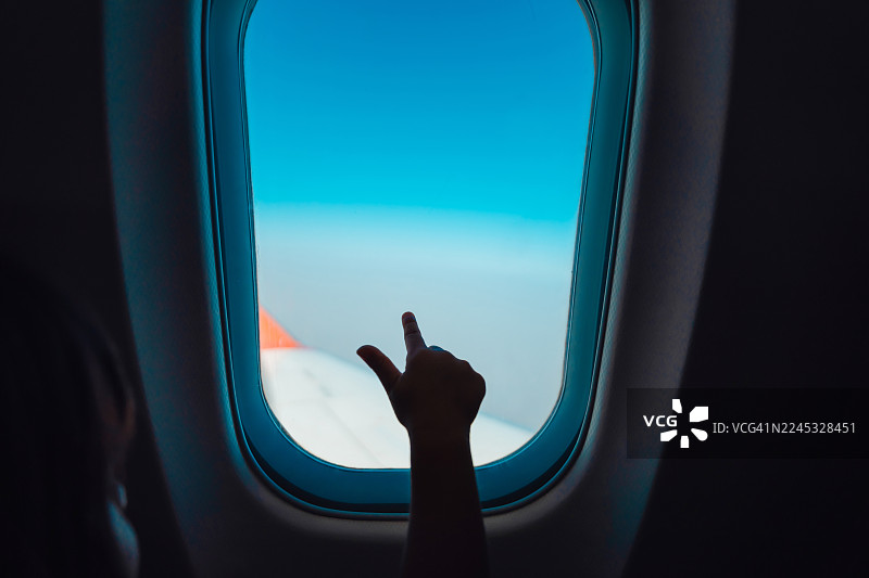 一只小手按在飞机舷窗上，指向天空中的云彩和景致图片素材