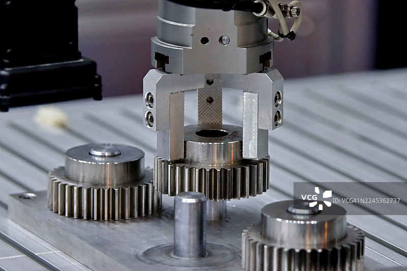 工业机器人。气动夹爪系统正在装配夹具上抓取并提升精密金属齿轮。图片素材