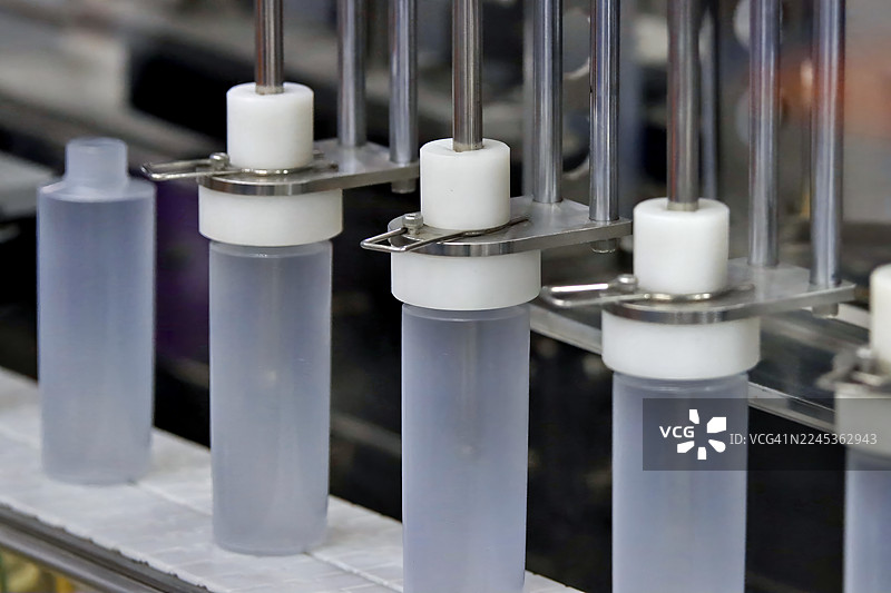 高速化妆品灌装线。磨砂半透明瓶子由不锈钢机械对齐以进行产品分配图片素材