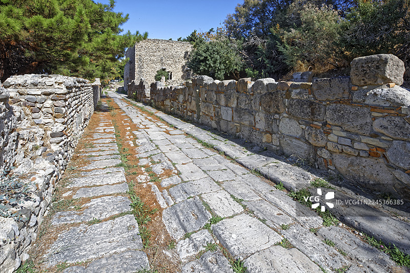 铺砌的道路，卡多路，建于公元前3世纪，由当地的杏仁石（一种凝灰岩）建造，留有古代车辆的痕迹，右后方是尼姆费翁（Nymphaeum），也称尼姆费安（Nymphaion），位于科斯市（Kos），科斯岛（Kos），多德卡尼斯群岛（Dodecanese Islands）的西部发掘区。图片素材