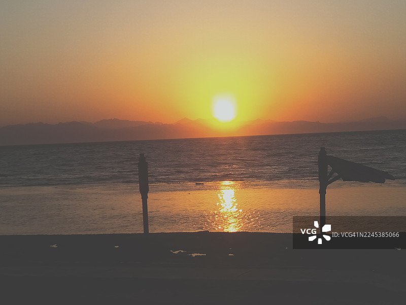 金色日落映照大海，远山绵延，宁静的海滩在前景中图片素材