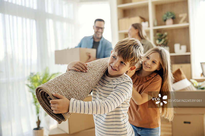 孩子们在新家搬地毯，父母则搬着箱子图片素材