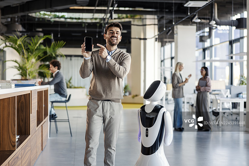 商务人士在办公室向机器人展示智能手机屏幕图片素材