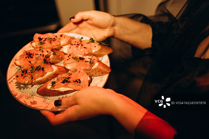 派对上，一只手递上三文鱼布鲁斯凯塔开胃菜图片素材
