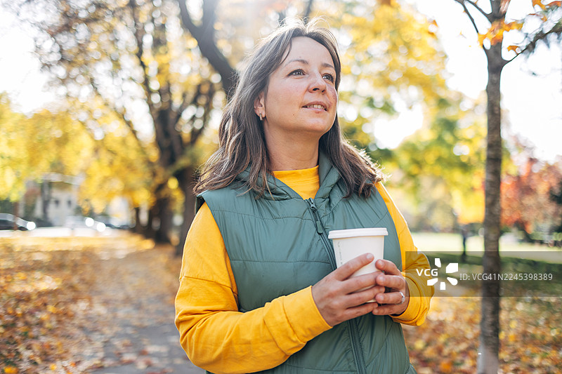 秋日公园里，一位女士边走边享受咖啡图片素材