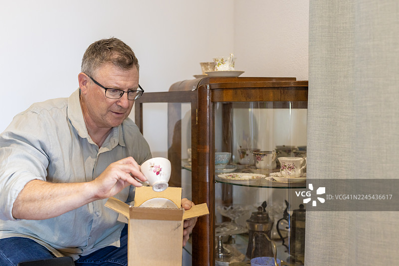 中年男子正在为他的收藏拆开一个新茶杯图片素材