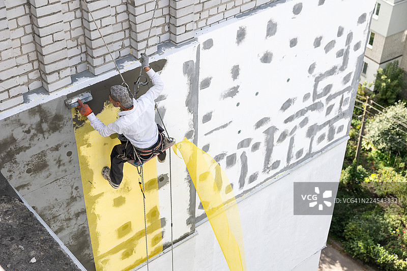 建筑工人正在用粘合剂覆盖钢筋网。他正在为建筑九楼的立面进行保温。图片素材