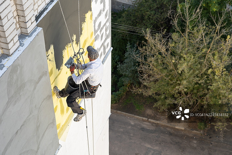 建筑工人正在用粘合剂覆盖钢筋网。他在建筑九楼进行外墙保温施工。图片素材
