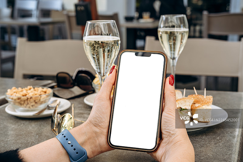 女式手机模型在咖啡馆的场景中，带有空白屏幕，周围是精致的饮品和美味的开胃菜，非常适合设计使用图片素材