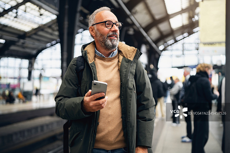 一位中年男士面带笑容，手持智能手机，站在柏林火车站。图片素材