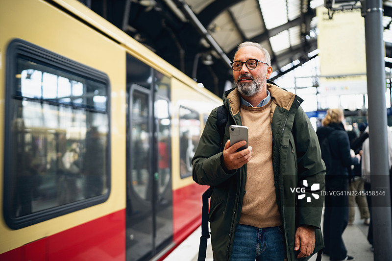 中年男子在柏林站台，身后火车驶过，他手中拿着智能手机图片素材