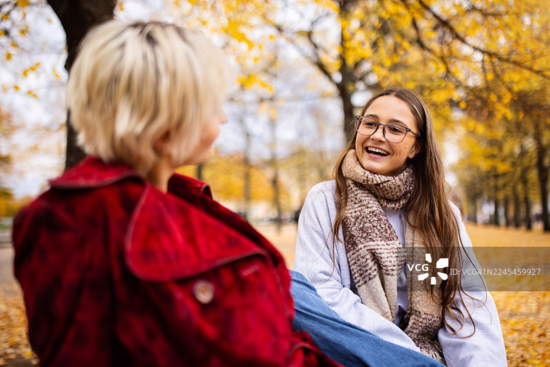 年轻女性朋友们坐在柏林公园里，周围是秋天的树木和落叶，她们在欢笑。图片素材