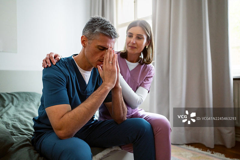 女护士与身穿手术服的男同事并排坐在床边，互相安慰图片素材