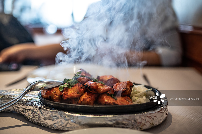 餐厅餐桌上冒着热气的坦都里烤鸡，香料味浓郁，烤得焦香，点缀着新鲜香草图片素材