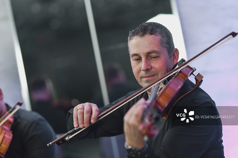 一位小提琴手正在进行现场音乐演奏，表情专注，弓法流畅。图片素材