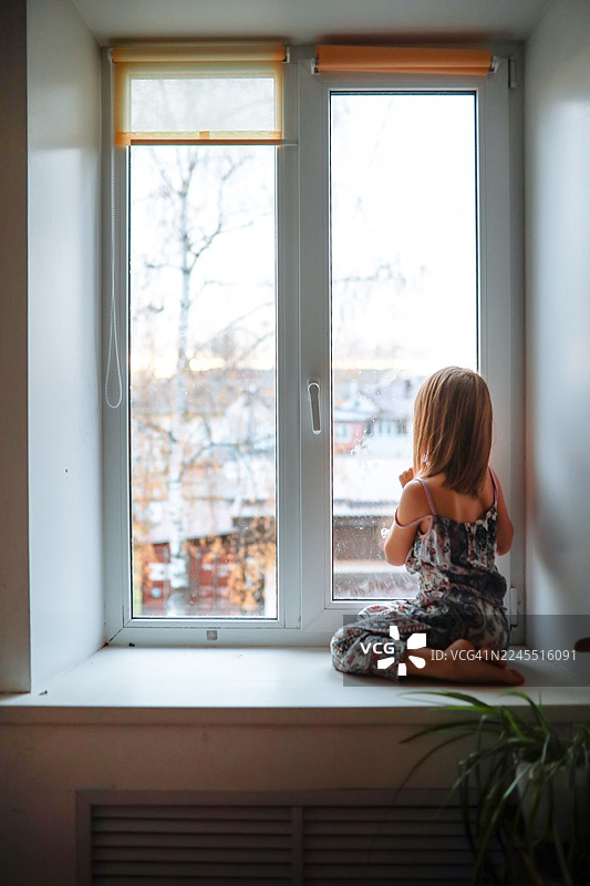 窗边等待的小女孩，坐在窗台上望着窗外，背面视图图片素材