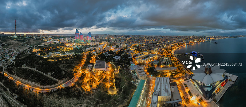 日落时分阿塞拜疆巴库火焰塔的鸟瞰图，城市天际线和闪耀的城市灯光在戏剧性的晚空中格外醒目。图片素材
