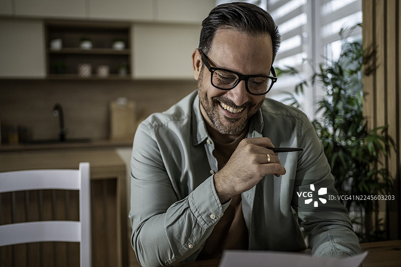 快乐的中年男子在家工作，微笑着审阅文件图片素材
