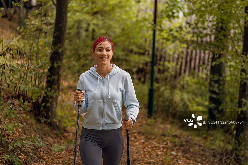 粉色头发的运动女孩在森林小路上用登山杖徒步图片素材