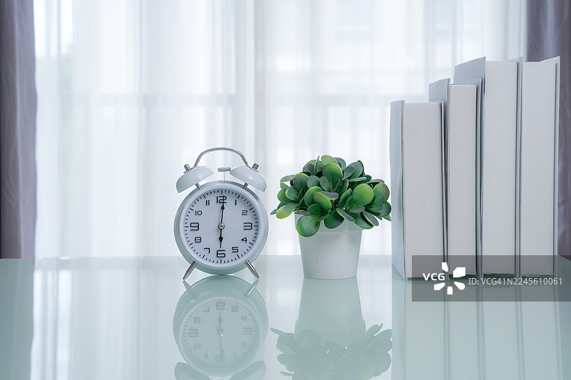摆放在桌子上的家居装饰。客厅室内设计，木制架子上放有闹钟和漂亮的盆栽植物。简约房间内的装饰品和书籍图片素材