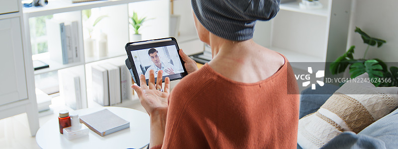 一位患有癌症的年长白人女性在家中通过数字平板电脑与医生进行视频通话。在线体检和年度检查。远程医疗和健康技术概念。图片素材