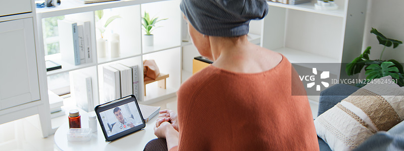 一位患有癌症疾病的老年白人女性在家中通过数字平板电脑与医生进行视频通话。在线体检和年度检查。远程医疗和健康技术概念。图片素材