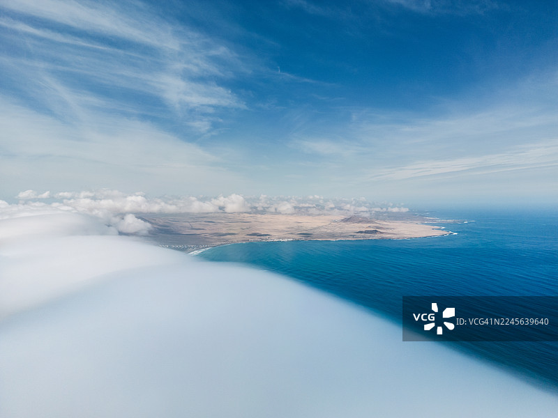 从低层云层边缘上方拍摄的航拍图，越过大西洋的一个海湾望向兰萨罗特海岸，西班牙加那利群岛图片素材