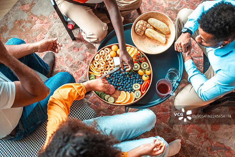 温馨客厅里，多元化的家庭围坐在熟食板周围欢聚图片素材