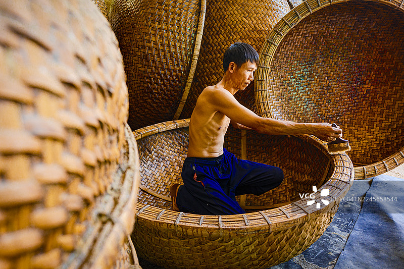 越南男子正在给竹筐船做防水处理图片素材