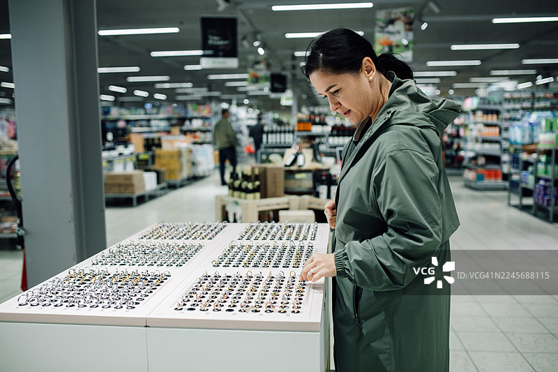 身穿绿色外套的女性在店内浏览珠宝戒指展示，顾客正在挑选戒指饰品类饰品图片素材