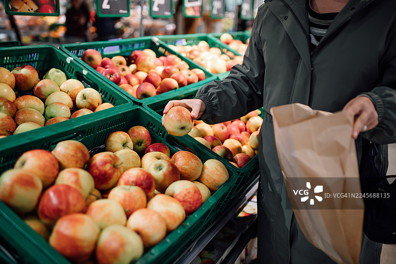 顾客在熙熙攘攘的菜市场绿色货箱里挑选新鲜苹果图片素材