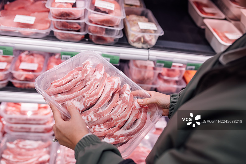 顾客在超市冷藏柜前挑选新鲜的猪肉片图片素材