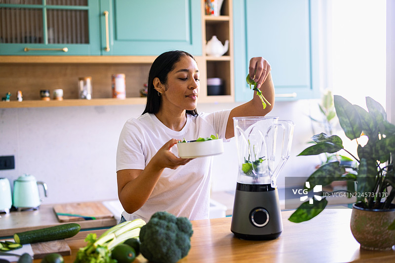 女子在现代厨房用搅拌机制作新鲜蔬菜绿色冰沙图片素材