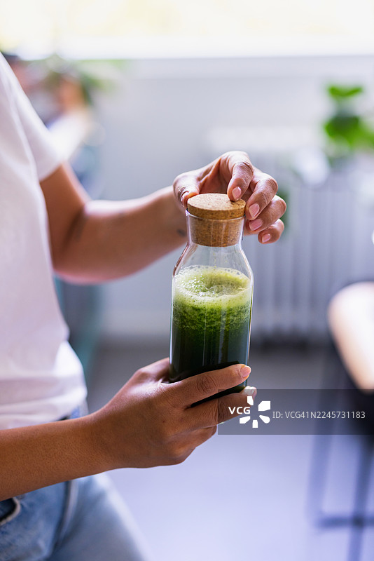 带软木塞的玻璃瓶装新鲜绿色冰沙放在明亮的厨房台面上图片素材