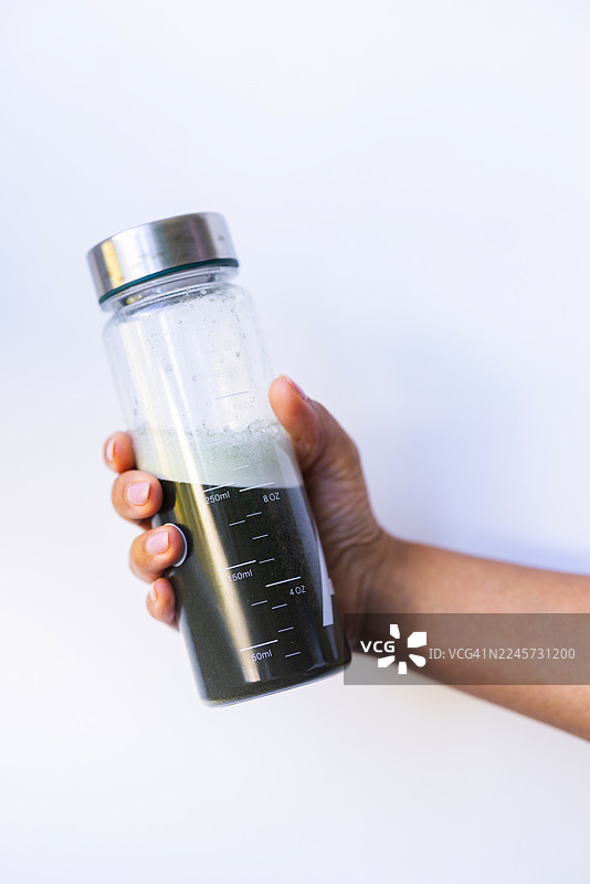 手持带有刻度线的深色液体玻璃瓶，用于健康饮品图片素材