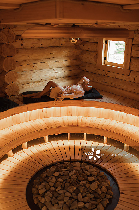 在传统的木制桑拿房中放松的人，配有石头加热器、金色灯光和舒适的长凳图片素材