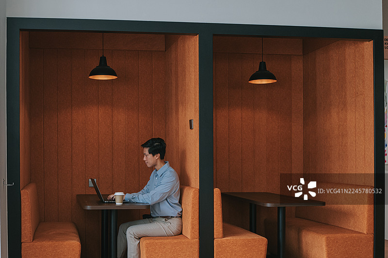 亚洲男子在现代共享办公隔间内独自工作图片素材