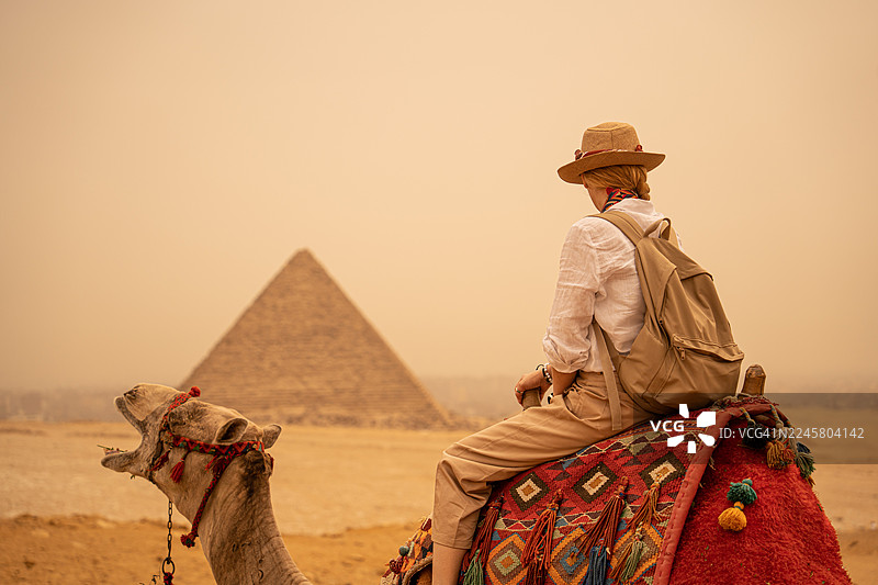 身穿度假服装的女性游客在吉萨金字塔前骑着骆驼旅行，埃及，开罗图片素材