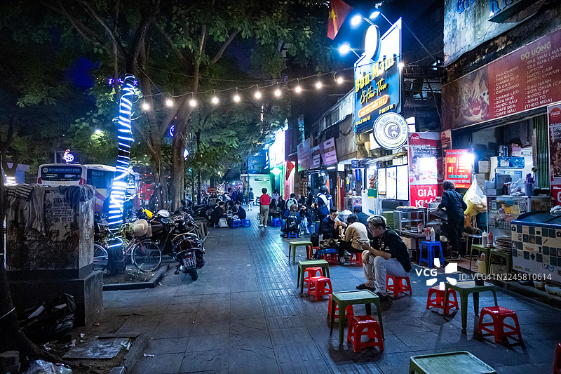 越南河内，路边餐厅在户外摆放着塑料桌椅，为享受热闹夜市氛围的食客们提供当地菜肴。图片素材