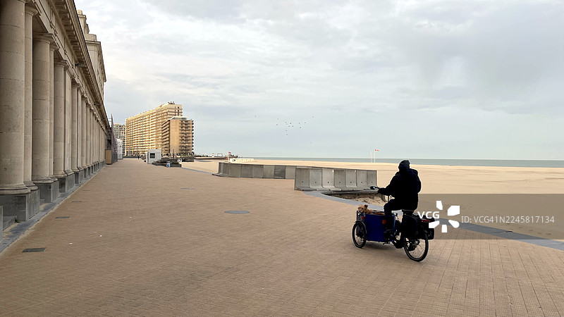 一名骑自行车的人经过奥斯坦德市皇家画廊翻新建筑工地的海滩景象。图片素材